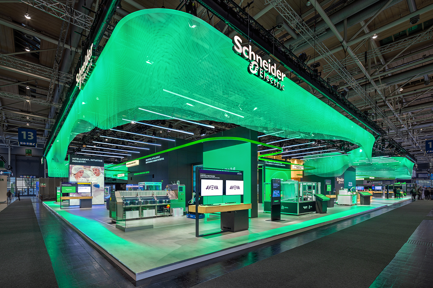 Perspektivische Außenansicht des Schneider Electric HMI 2026 Standes mit Halle 13 Wegweiser und leuchtender Deckenwelle.