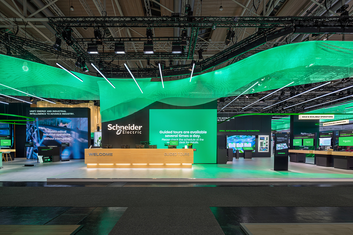 Frontaler Empfangsbereich Welcome und Guided Tours Counter von Schneider Electric auf der HMI 2026 mit Holzfurnier und LED-Wall.