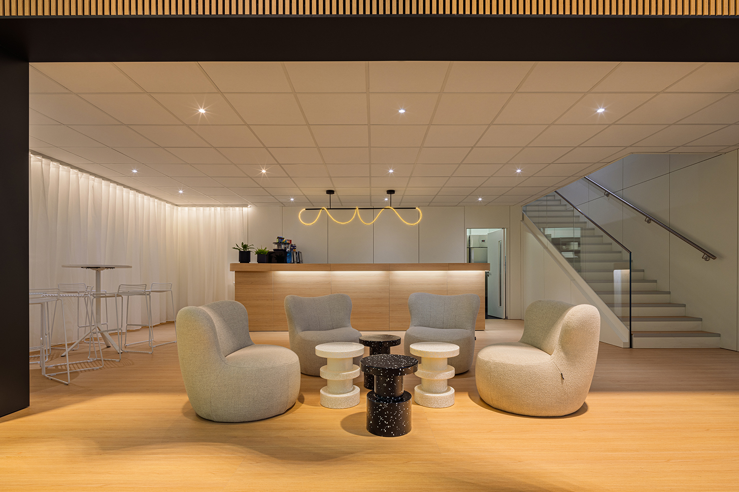 Interieur der VIP-Lounge unter dem Doppelstock mit geschwungener LED-Leuchte, Sesselgruppe, Bar und Treppenaufgang.