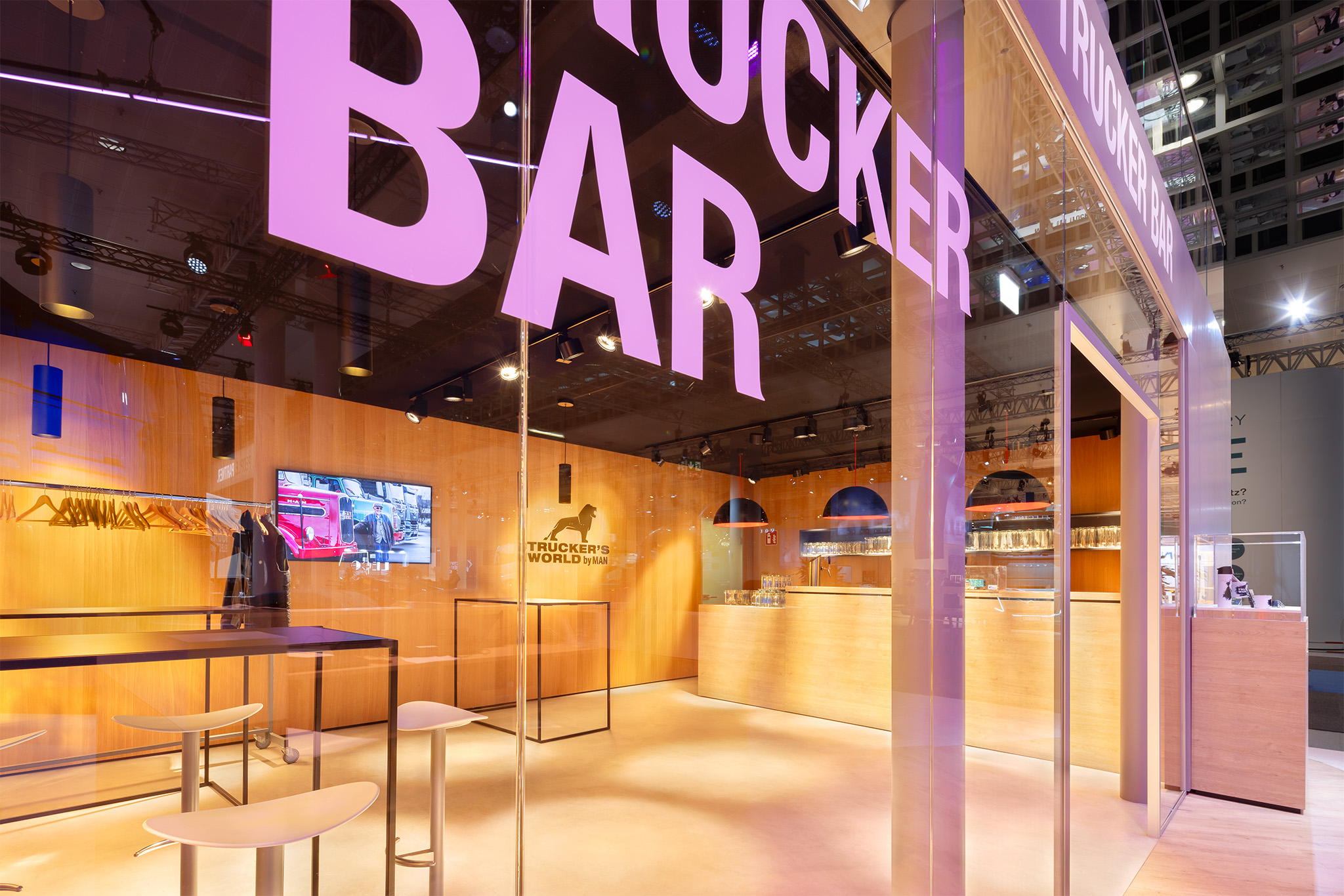 Trucker Bar Lounge mit lila Neon-Schriftzug und Sitzecken auf dem MAN Messestand.