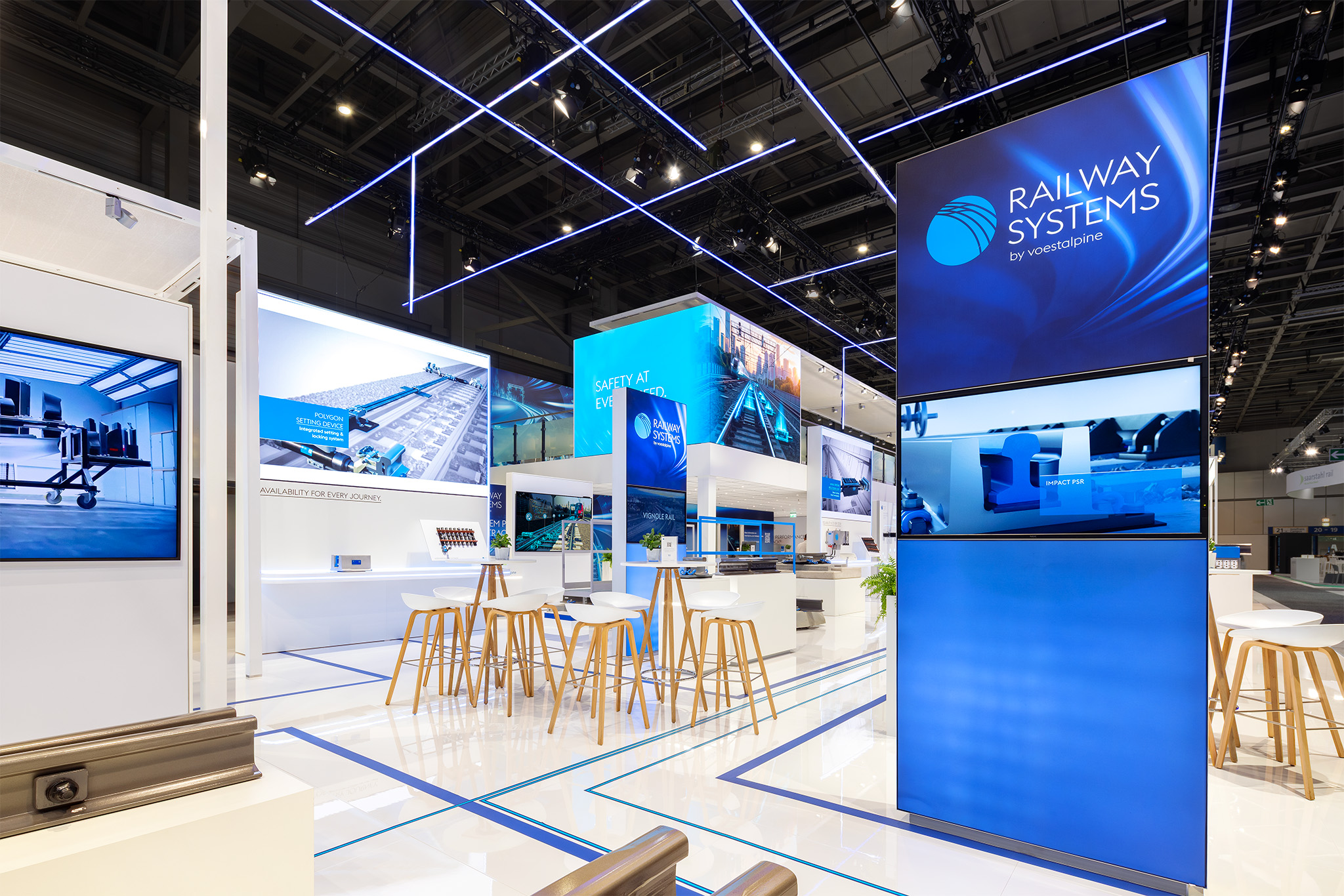 Detailansicht des InnoTrans 2026 Messestands von voestalpine Railway Systems mit Medienwänden und Stehtisch-Lounge von Raumtechnik.